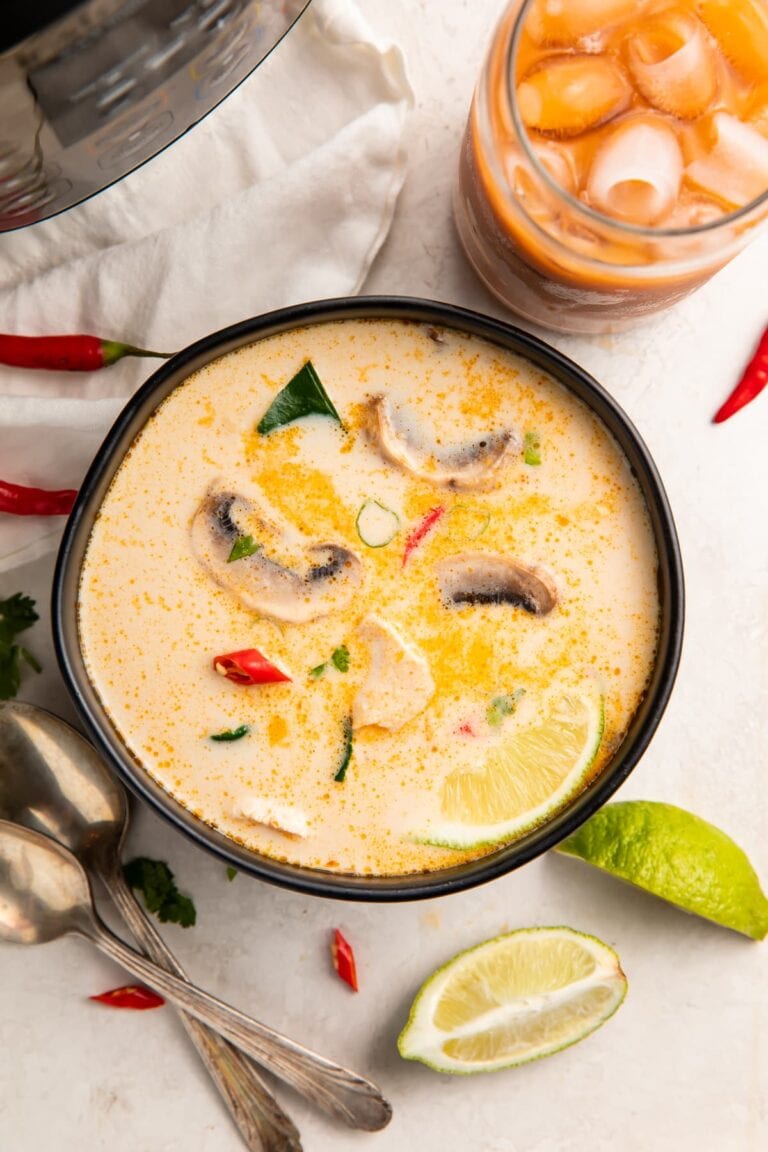 Overhead view of Instant Pot tom kha soup in a black bowl surrounded by limes and peppers