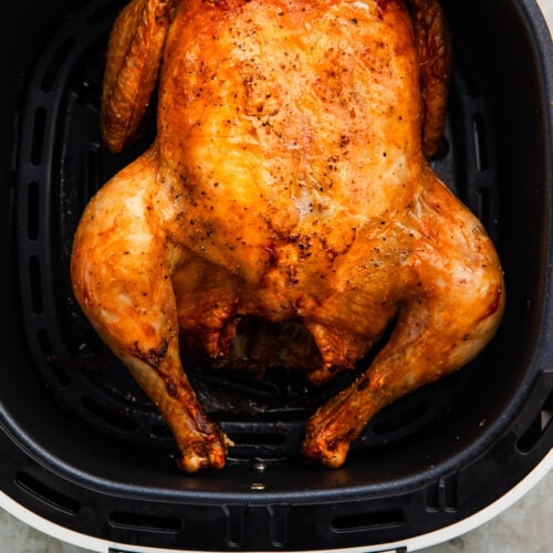 A whole chicken cooked in and resting in an air fryer basket.