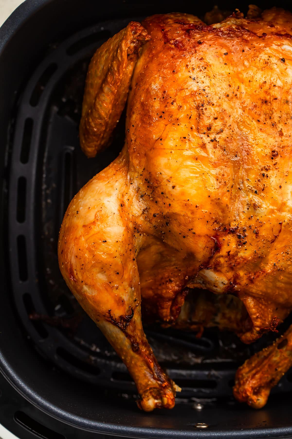 A whole chicken cooked in and resting in an air fryer basket.