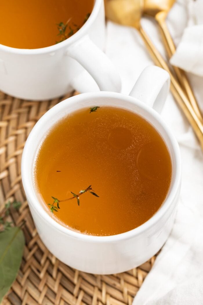 beef consommé in two mugs with fresh thyme on top