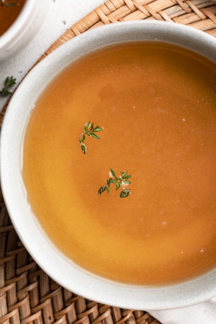 beef consommé in a bowl with fresh thyme on top