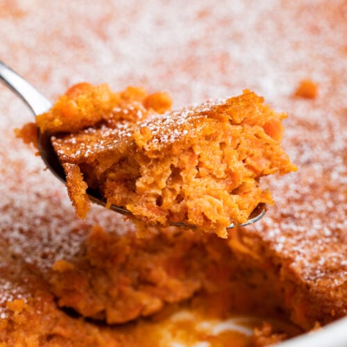 A spoonful of carrot soufflé being lifted out of a casserole dish