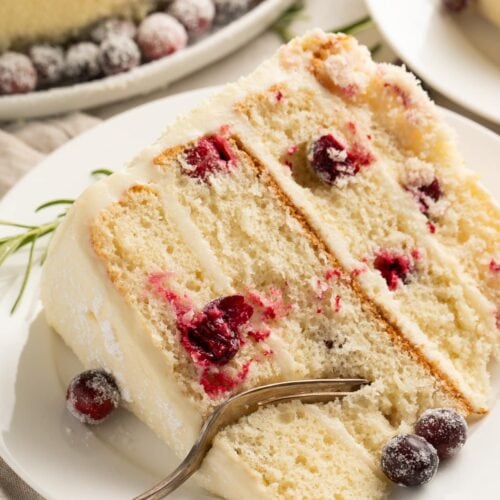 A slice of cranberry white chocolate cake on a white plate with a fork