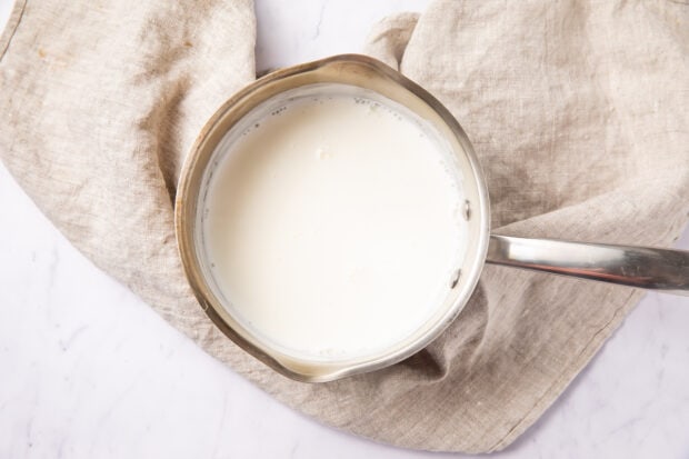 Hot milk in a small saucepan on a white surface with a neutral linen