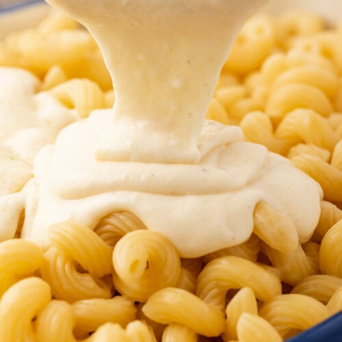 Mornay sauce being poured over a bowl of spiral noodles