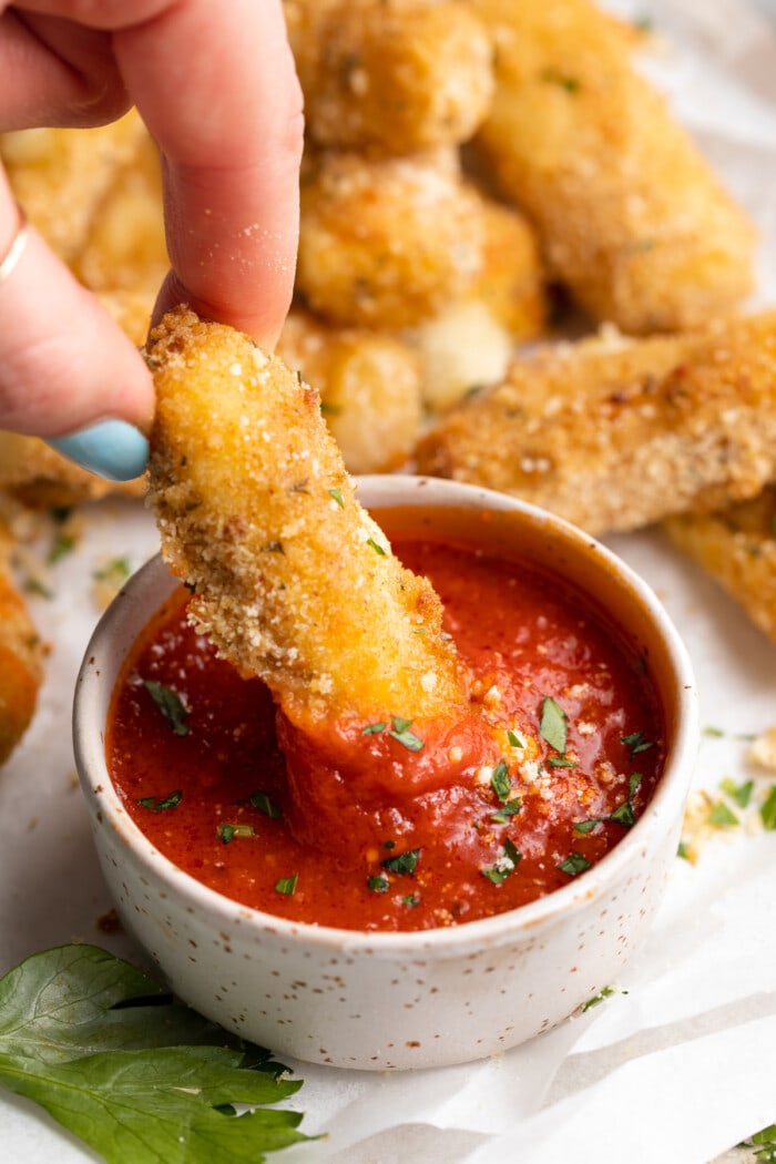 air fryer mozzarella stick being dipped into marinara sauce