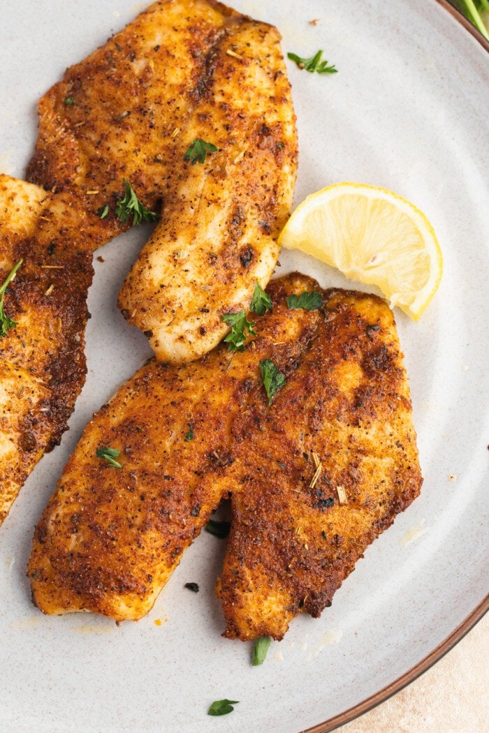 Overhead view of air fried tilapia fillets on a white plate.