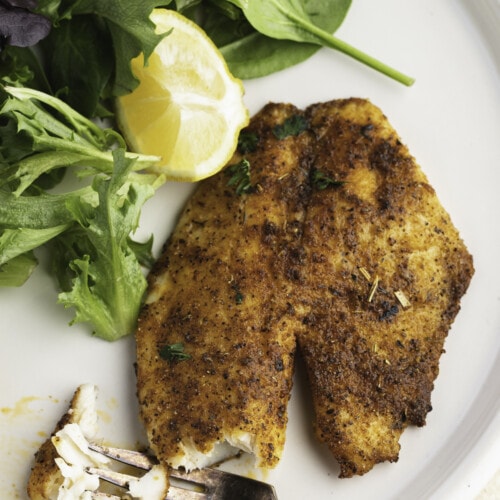 Overhead view of air fryer tilapia on a plate with broccoli and a lemon wedge.