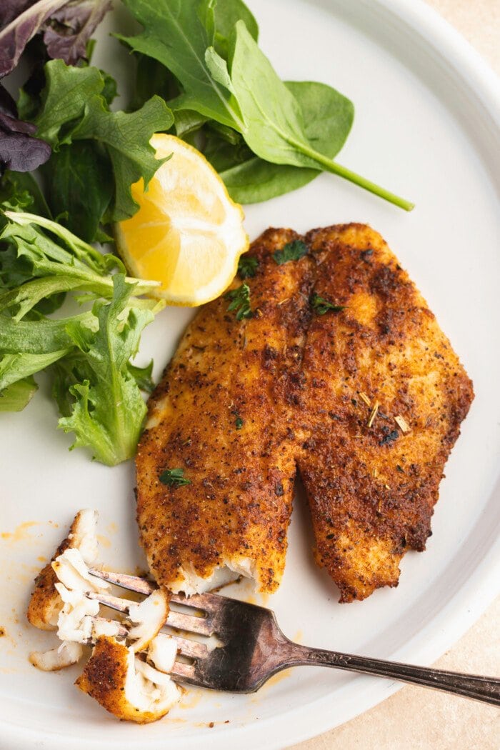 Overhead view of air fryer tilapia on a plate with broccoli and a lemon wedge.