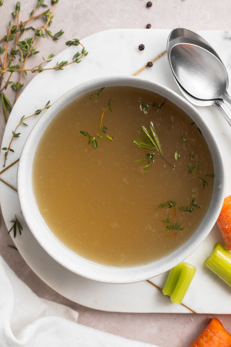 overhead image of a bowl of stovetop bone broth with fresh herbs on an oval platter.