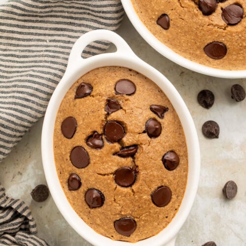 Top-down, overhead view of two oblong single-serve ramekins holding fluffy blended baked oats dotted with chocolate chips.