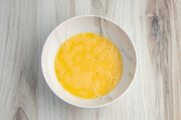 Egg wash in shallow bowl on a light neutral countertop.