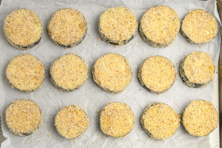 Breaded eggplant discs on a baking sheet lined with parchment paper.