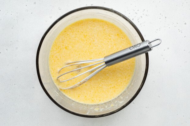 Overhead view of wet ingredients for gluten-free donuts in large glass bowl with whisk.