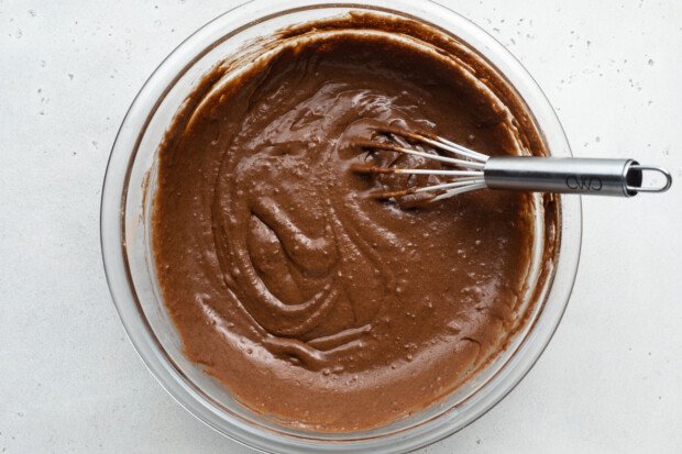 Overhead view of chocolate gluten-free donut batter in large glass mixing bowl with metal whisk.