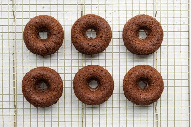 Overhead view of 6 baked chocolate gluten-free donuts on a wire cooling rack.