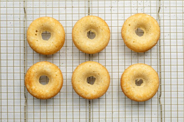 Overhead view of 6 baked chocolate gluten-free donuts on a wire cooling rack.