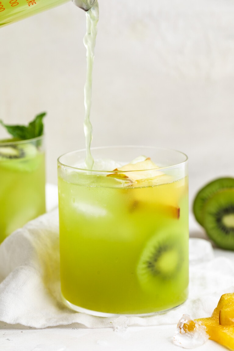 Lime green kiwi starfruit refresher poured into a glass with ice and slices of starfruit and kiwi.