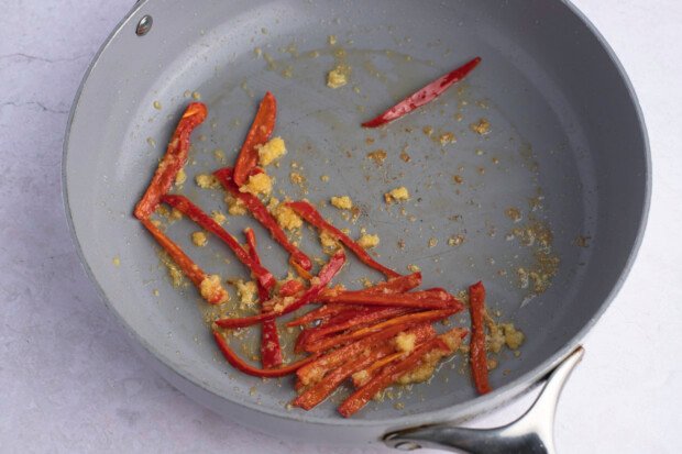 Red chilis, minced garlic, and grated ginger in large grey skillet on white background.