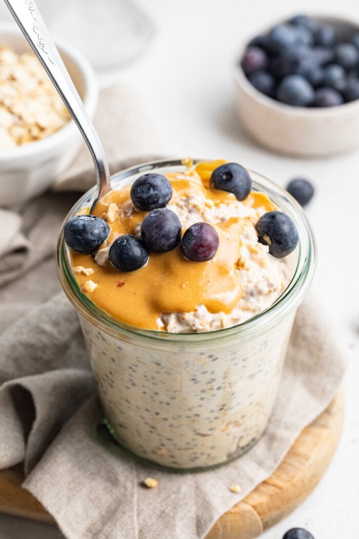 Overhead, 3/4-angle view of peanut butter overnight oats topped with blueberries on a wooden serving board.