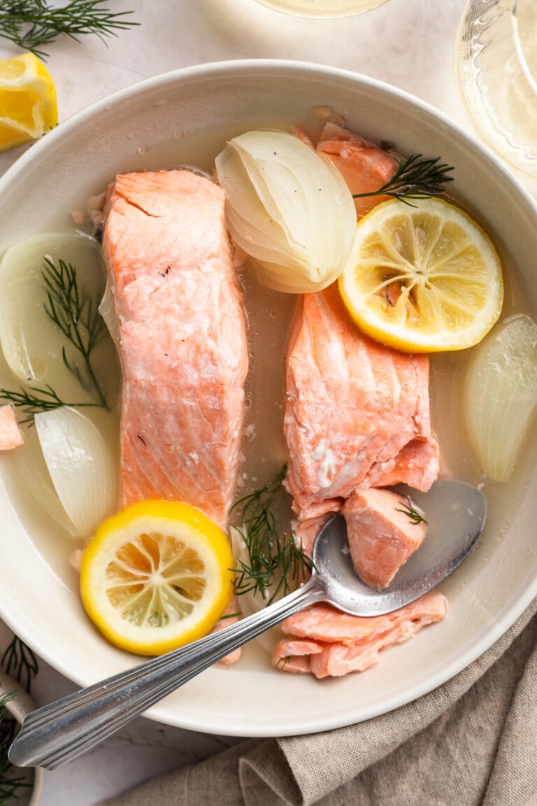 Overhead view of poached salmon with lemon and onion in a bowl.