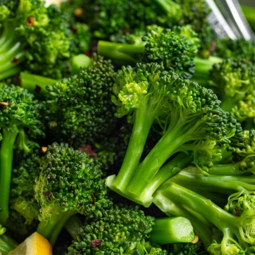 Close-up view of steamed broccoli florets with lemon wedges in a large bowl.