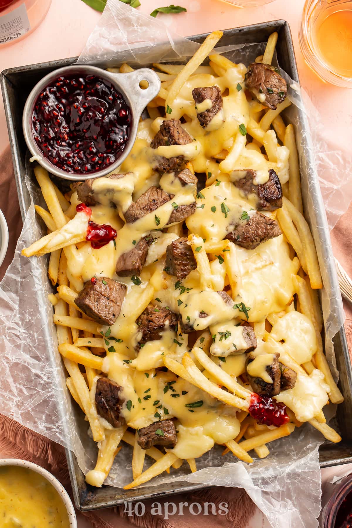 Overhead, angled view of baked brie and steak cheese fries in a rectangular deep pan with raspberry preserves.