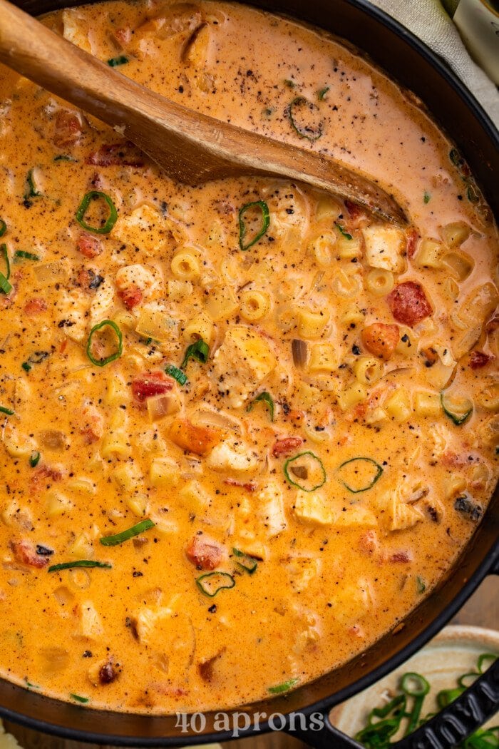 Overhead view of a giant pot of creamy cajun chicken pasta soup with a wooden spoon.