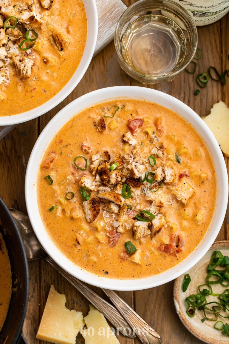 Overhead view of one bowl and one partial bowl of cajun chicken pasta soup on a wooden table.