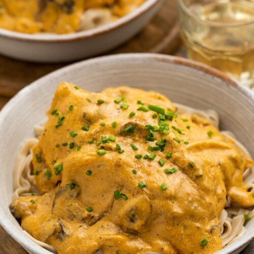 3/4-angle view of two bowls of Crockpot angel chicken served over a bed of pasta with a glass of water.