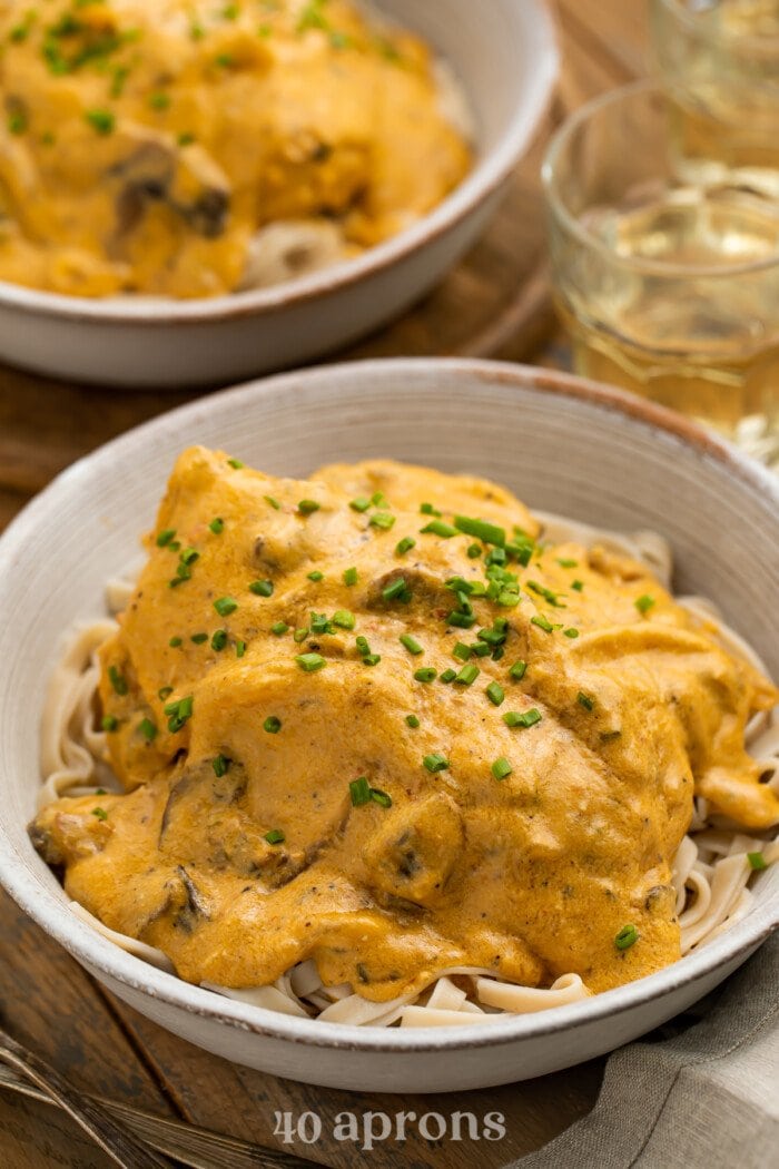 3/4-angle view of two bowls of Crockpot angel chicken served over a bed of pasta with a glass of water.