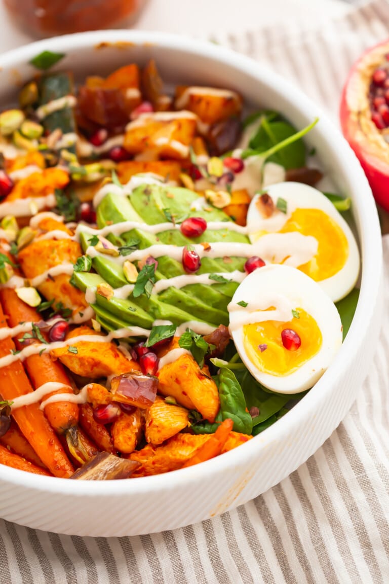 Angled 3/4 view of a harissa nourish bowl with eggs and avocado on a neutral striped cloth napkin.