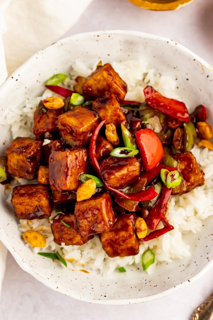 Overhead view of kung pao tofu with stir-fried veggies and white rice in a white bowl.