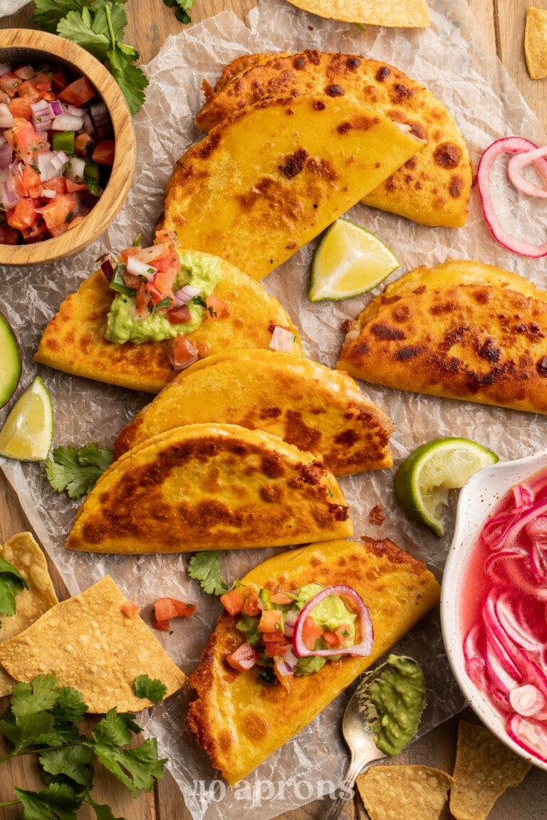 Overhead view of crispy cheesy refried bean tacos on parchment paper covering a wooden table with pico and cilantro.