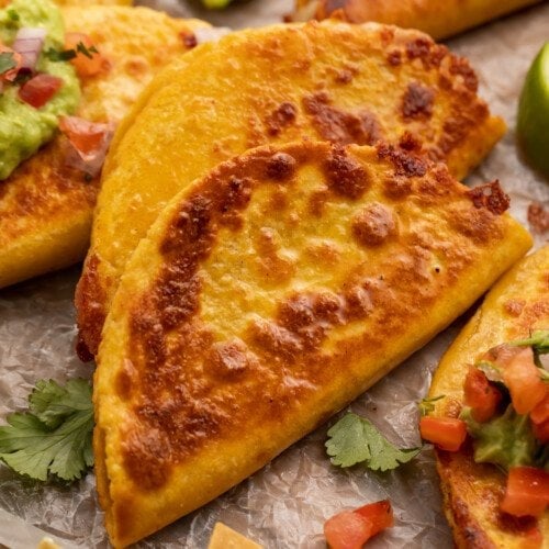 Closeup view of a crispy, cheesy, refried bean taco on parchment paper with pico and cilantro.