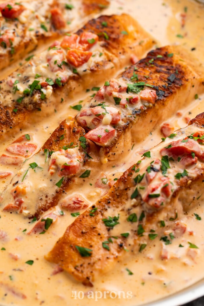 Overhead close-up of 3 salmon fillets in a silver saucepan with a creamy sauce.