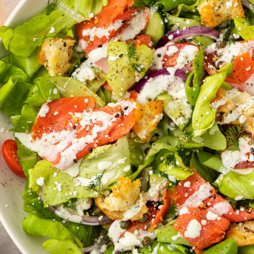 Overhead, close-up view of a smoked salmon bagel salad in a white bowl.