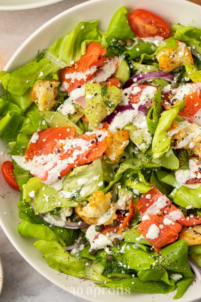 Overhead, close-up view of a smoked salmon bagel salad in a white bowl.