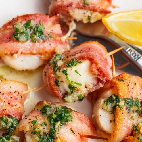 Overhead view of bacon wrapped scallops with herb butter sauce on a white plate with a fork.