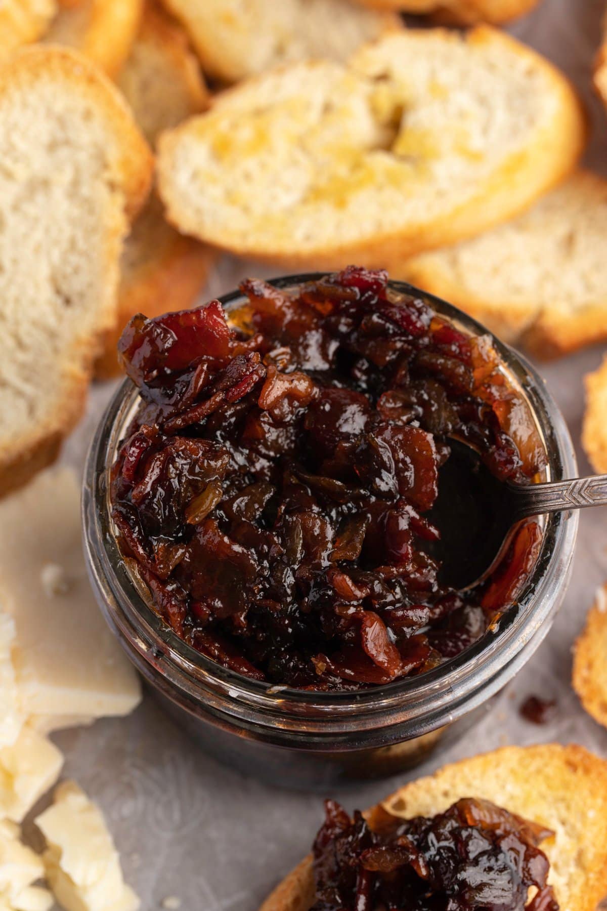 Overhead view of a jar of bacon jam surrounded by slices of crisp bread.