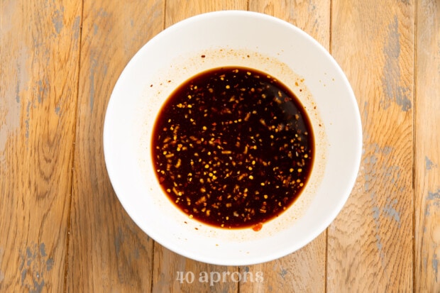 Overhead view of a white mixing bowl with bourbon chicken sauce on a wooden table.