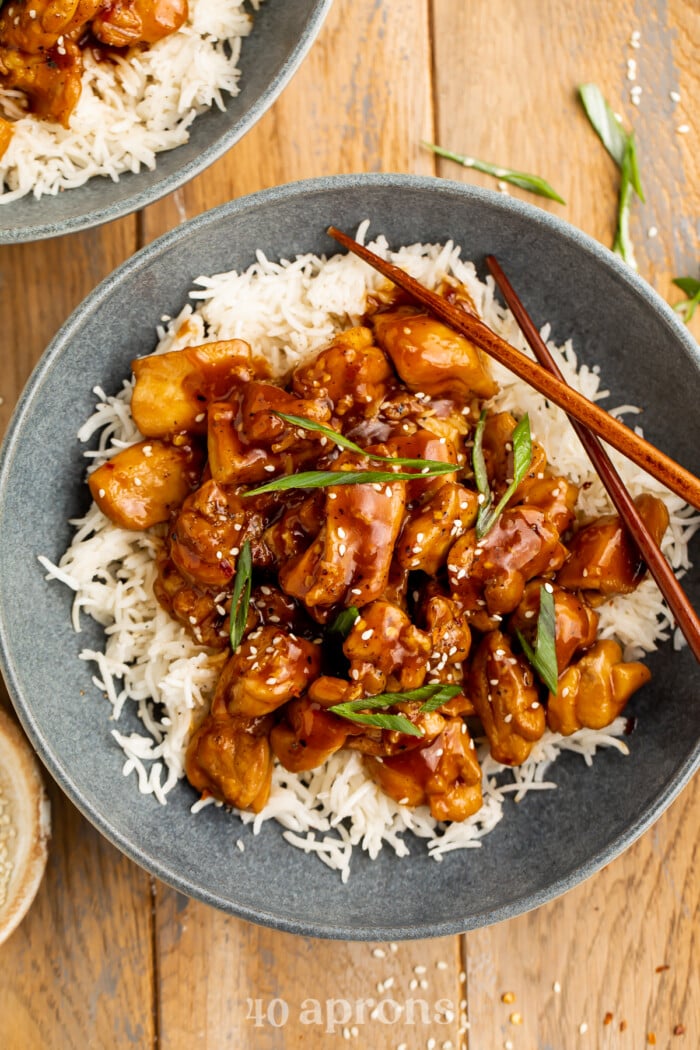 Overhead view of a dark blue-grey bowl of white rice topped with Bourbon Chicken and chopped green onions.