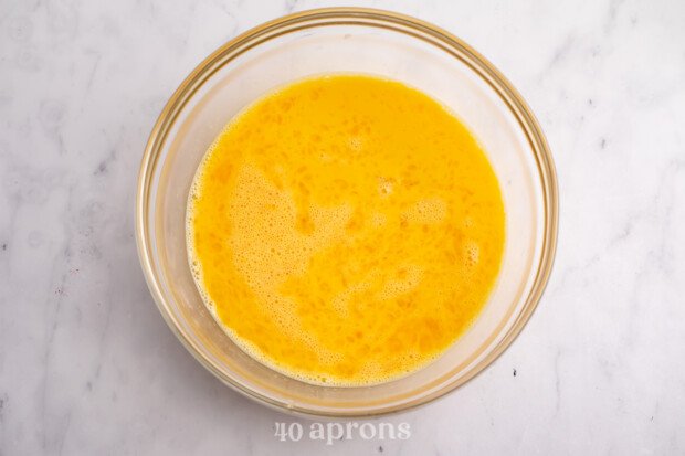 Scrambled egg and cream mixture in large glass mixing bowl on neutral countertop.