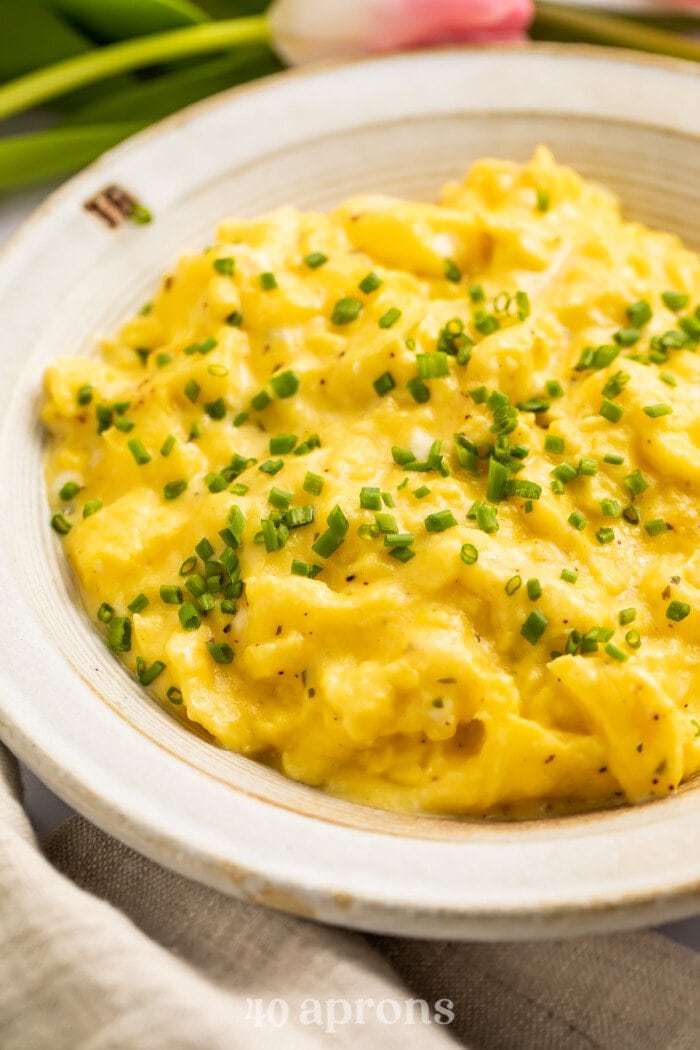 3/4-angle view of a bowl of boursin scrambled eggs garnished with chives.