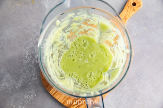 Overhead view of cucumber juice in glass blender on wooden board.