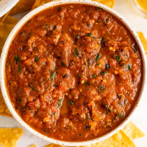 Overhead view of a bowl of red roasted salsa surrounded by tortilla chips.