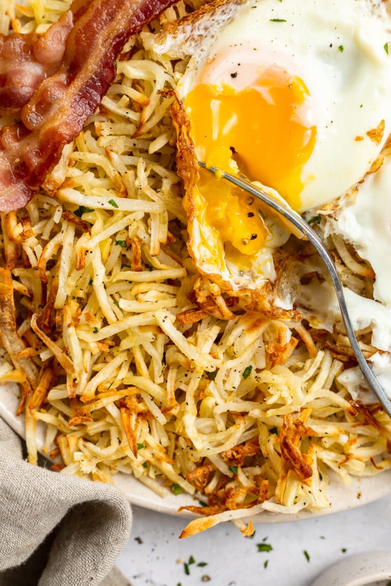 Close-up view of air fryer hashbrowns on a plate with bacon and an egg.