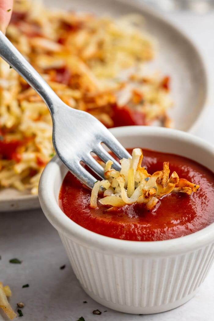 Air fryer hashbrowns on a fork being dipped into a small ramekin of chipotle ketchup.