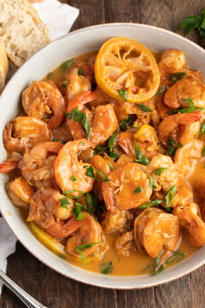 Overhead, zoomed out view of a large bowl of BBQ shrimp with crusty bread.