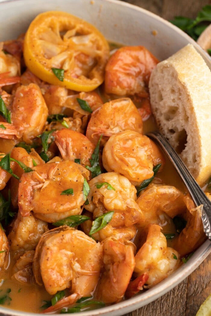 Overhead view of a bowl of BBQ shrimp with crusty bread.